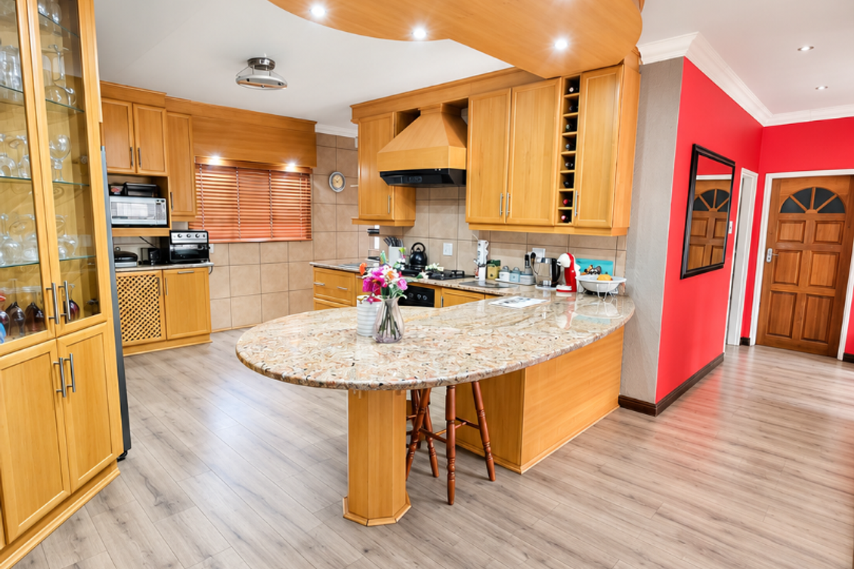 Spacious kitchen featuring warm wooden cabinetry, a large granite-topped island, recessed lighting, and modern laminate flooring, creating a functional and inviting culinary space.