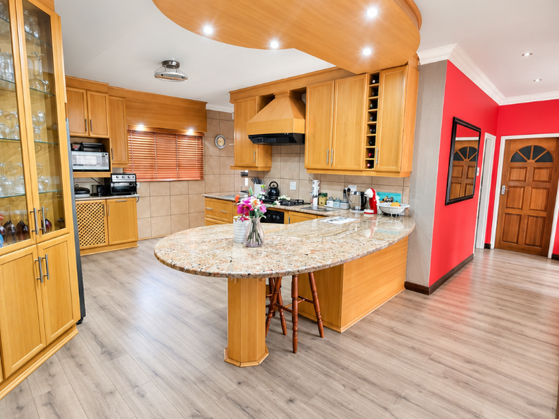 Spacious kitchen featuring warm wooden cabinetry, a large granite-topped island, recessed lighting, and modern laminate flooring, creating a functional and inviting culinary space.