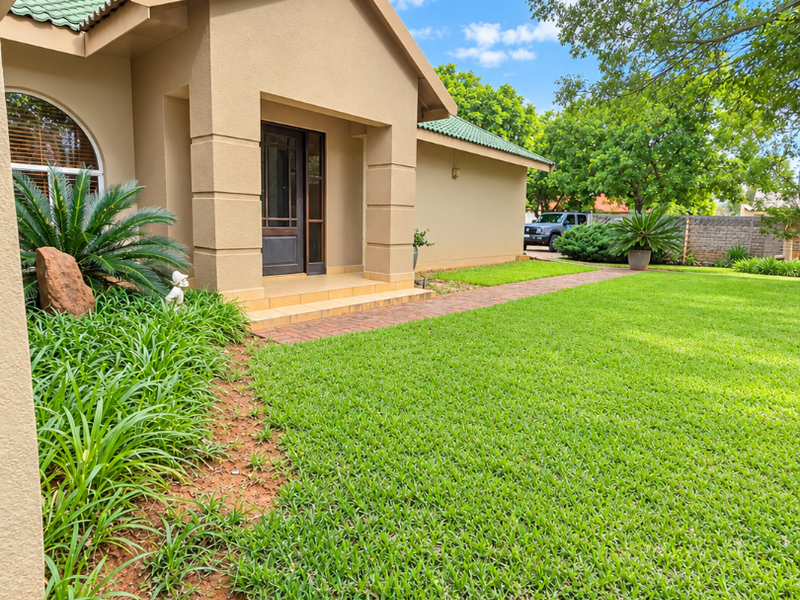 A well-maintained front entrance featuring a covered porch, brick walkway, and manicured lawn with established garden landscaping.