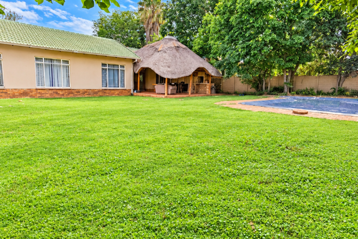 Spacious rear garden featuring a large lawn, a swimming pool with cover, and a traditional thatched roof lapa entertainment area.