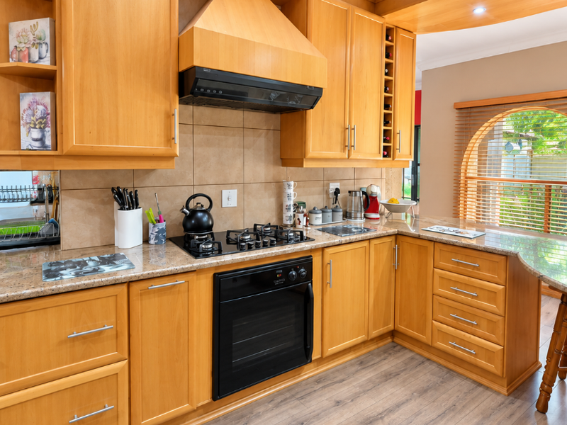 A well-maintained kitchen featuring warm wooden cabinetry, granite countertops, built-in oven, gas hob, and an elegant arched window with timber blinds.