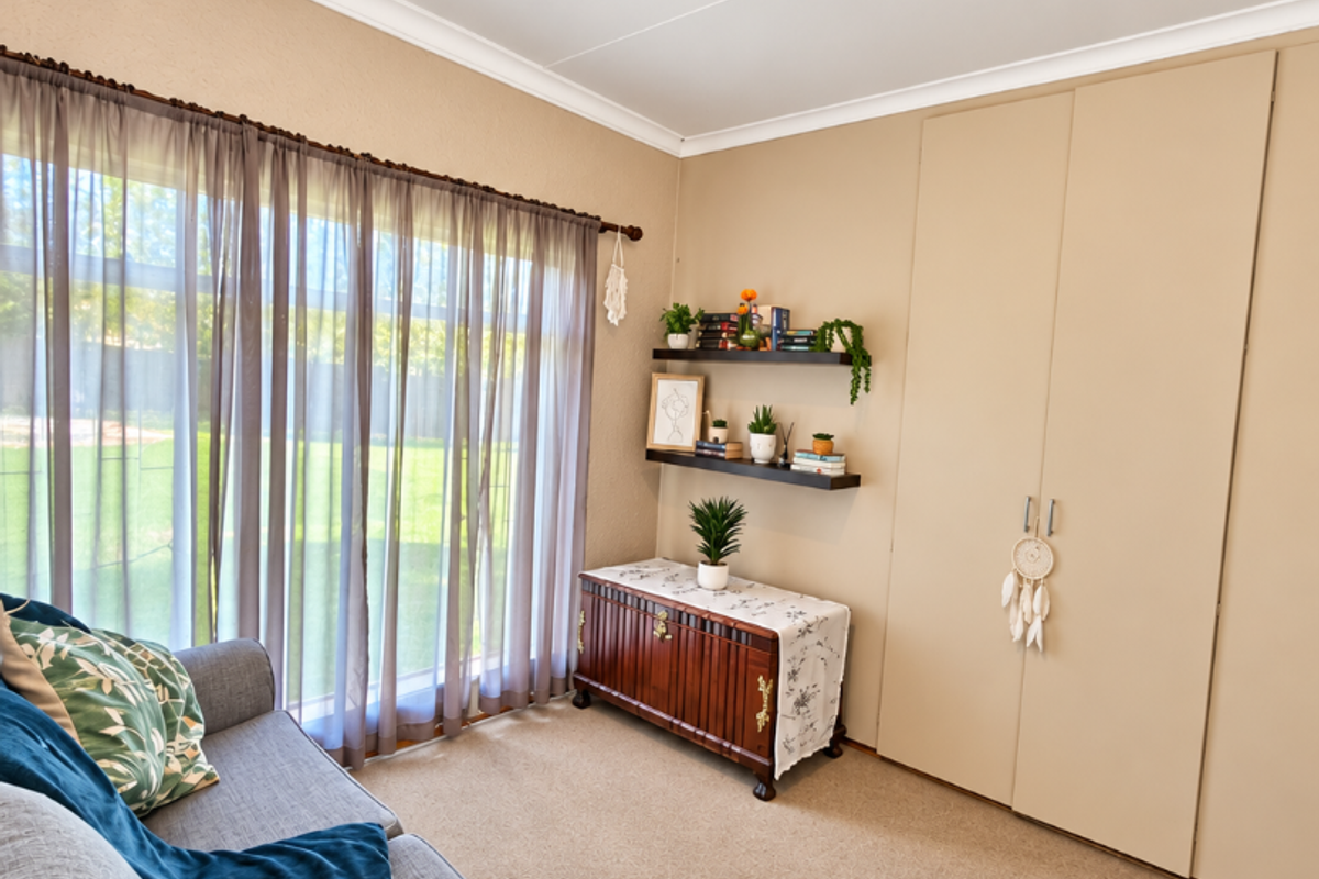 A well-maintained bedroom featuring neutral walls, carpeted flooring, and ample built-in cupboard storage with natural light from the large window.