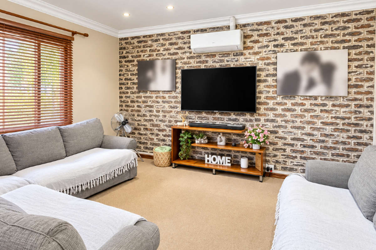 A comfortable living room featuring an exposed brick feature wall, recessed downlighting, and a wall-mounted split-system air conditioner.