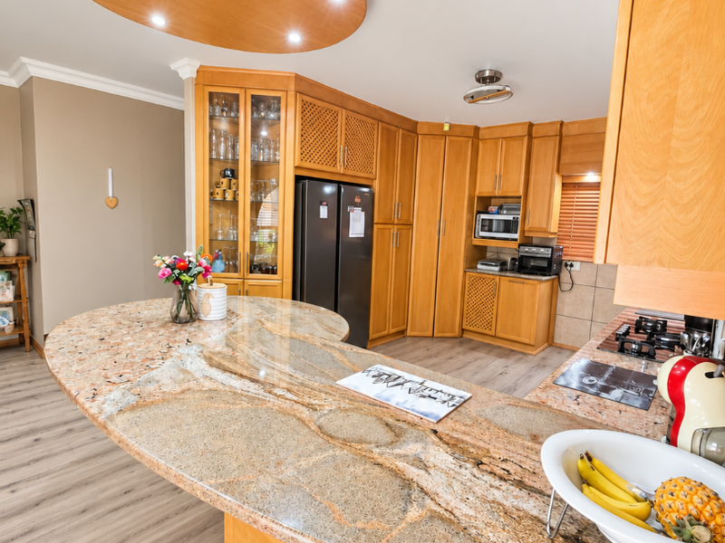 Spacious kitchen featuring extensive wooden cabinetry, a large curved granite island, and integrated appliances under a unique circular recessed ceiling feature.