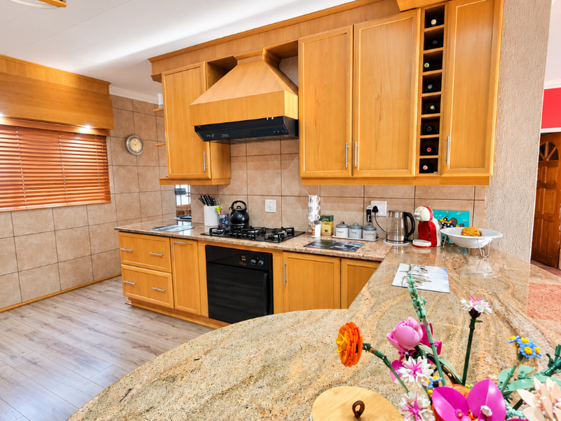 A well-maintained kitchen featuring warm wooden cabinetry, granite countertops, a gas hob with extractor fan, and integrated wine storage.