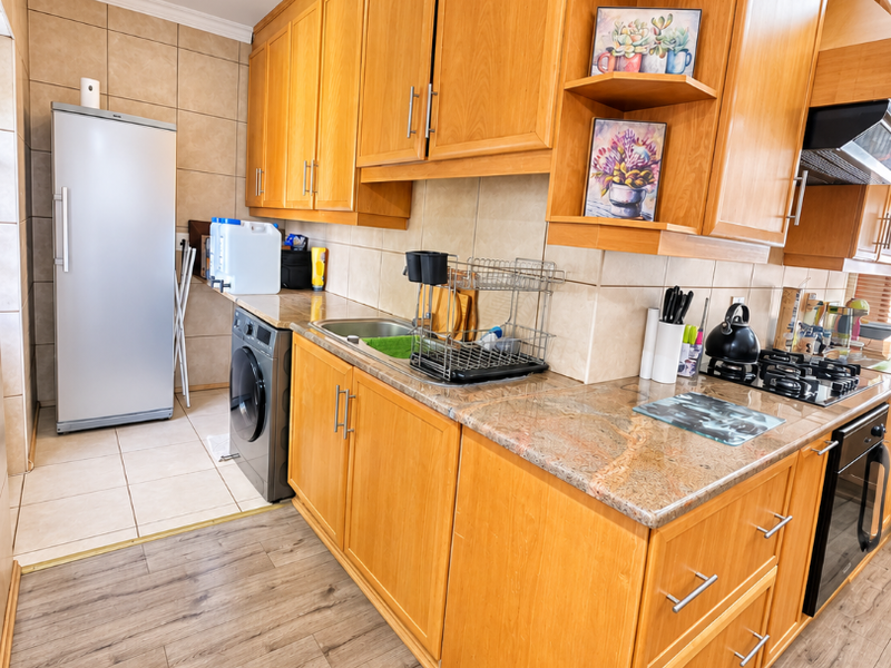 A functional kitchen featuring warm wooden cabinetry, granite countertops, integrated appliances including an oven and hob, and a tiled backsplash with durable laminate flooring.