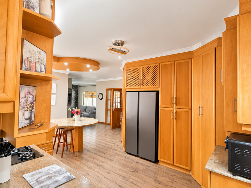 Spacious open-plan kitchen featuring warm-toned wooden cabinetry, granite countertops, and integrated appliances, flowing seamlessly into the adjacent living and dining area.