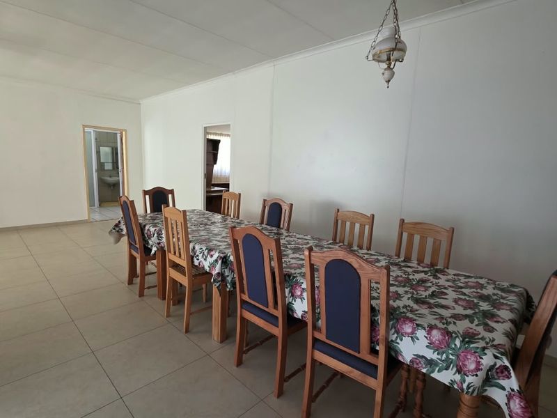 A spacious dining area featuring neutral tiled flooring, a ceiling fan, and a central pendant light fixture, providing a functional space for gatherings.