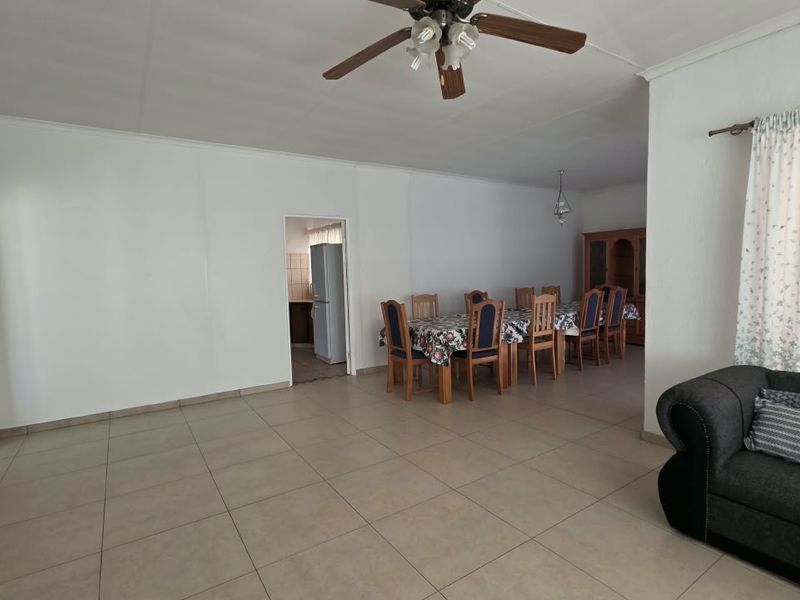 Spacious open-plan living and dining area featuring neutral tiled flooring, coved cornicing, and a central ceiling fan, providing a versatile layout for commercial use.