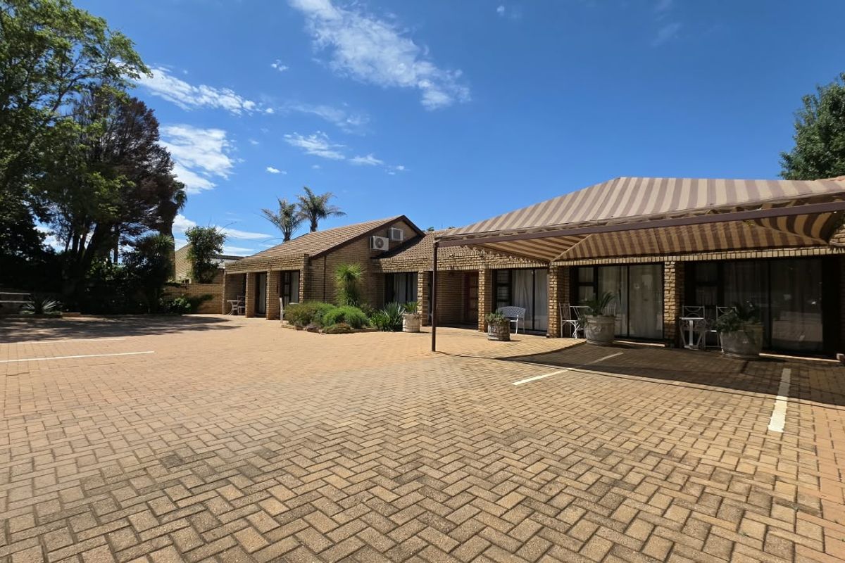 Rear exterior view of a commercial property featuring a large paved courtyard, face brick facade, and a covered patio area with striped awning.