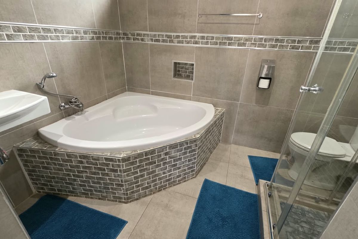 A modern bathroom featuring a corner bathtub, a separate glass-enclosed shower, a wall-mounted basin, and a toilet, finished with neutral wall and floor tiling.