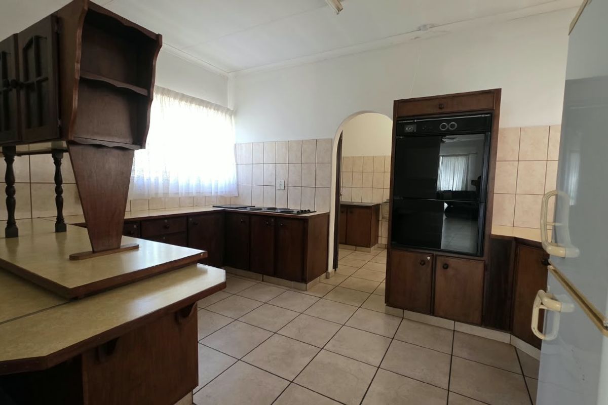A functional kitchen featuring dark wood cabinetry, tiled flooring, a built-in oven, and a tiled backsplash, with an arched doorway leading to an adjacent space.