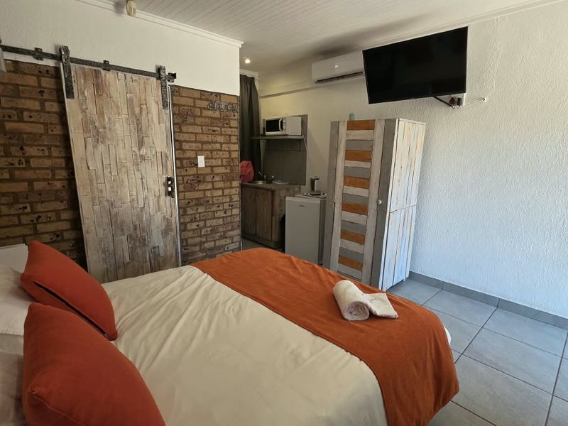 A bedroom featuring an exposed brick wall, sliding barn door, tiled flooring, and a compact kitchenette area with air conditioning.