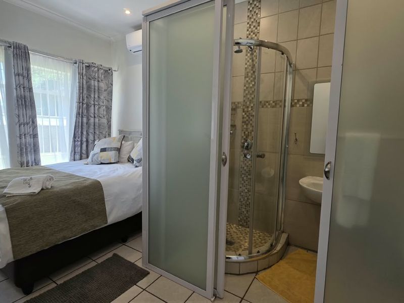 A bedroom featuring an integrated en-suite shower with frosted glass enclosure, tiled flooring, and a wall-mounted air conditioning unit.
