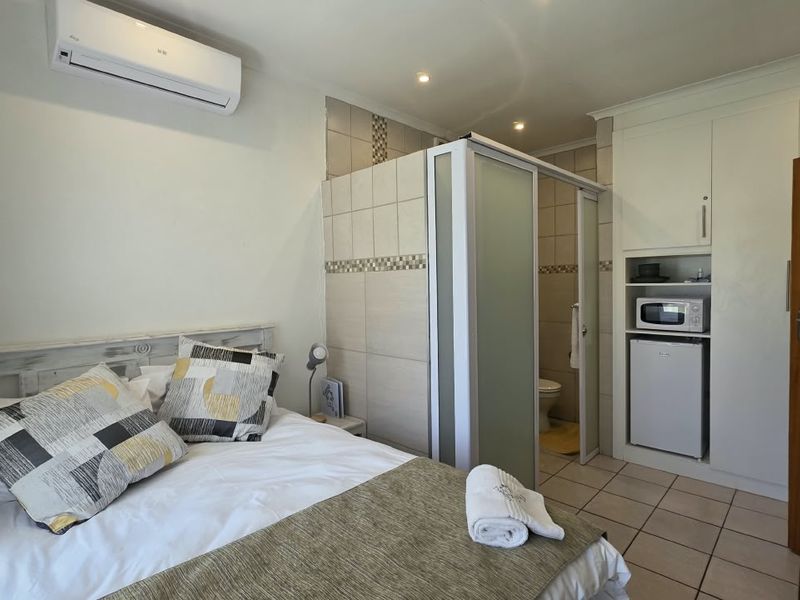 A well-maintained bedroom featuring tiled flooring, built-in cabinetry, a split-system air conditioner, and an integrated en-suite bathroom partition.