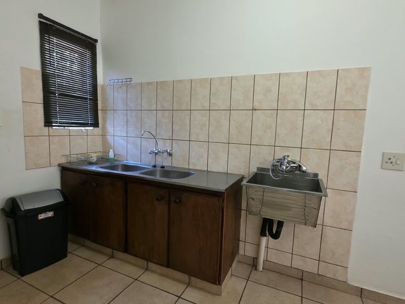 A functional scullery area featuring a stainless steel double sink, a separate wall-mounted utility sink, wooden cabinetry, and tiled finishes.