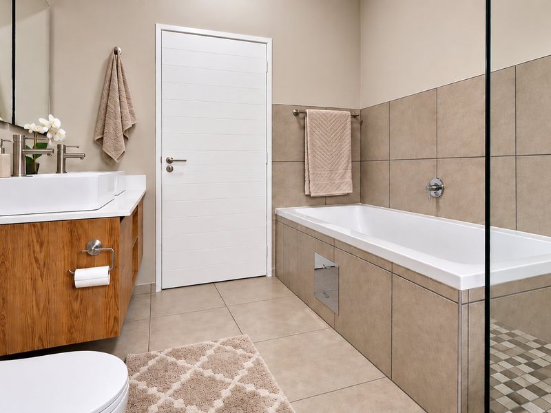 Modern bathroom featuring a vessel sink on a wood-finish vanity, a tiled built-in bathtub, and a glass-enclosed shower area with neutral finishes.