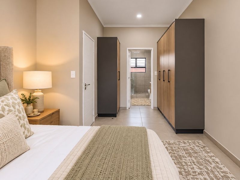 A well-maintained bedroom featuring modern built-in cupboards, neutral tiled flooring, and direct access to an en-suite bathroom.