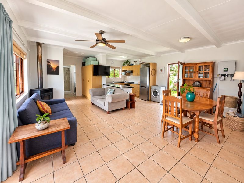 Spacious open-plan living area featuring tiled floors, exposed beam ceilings, a wood-burning fireplace, and an integrated kitchen with functional cabinetry.
