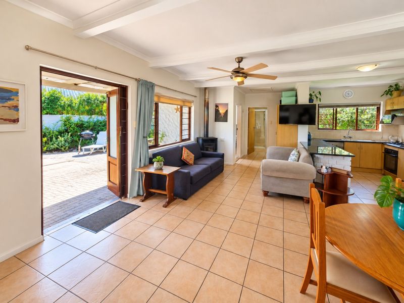 Open-plan living and kitchen area featuring tiled floors, a wood-burning fireplace, and direct access to an outdoor patio through double doors.