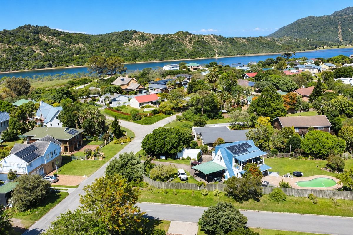 An aerial view of a residential neighborhood featuring homes with solar panels, swimming pools, and lush green surroundings near a river.