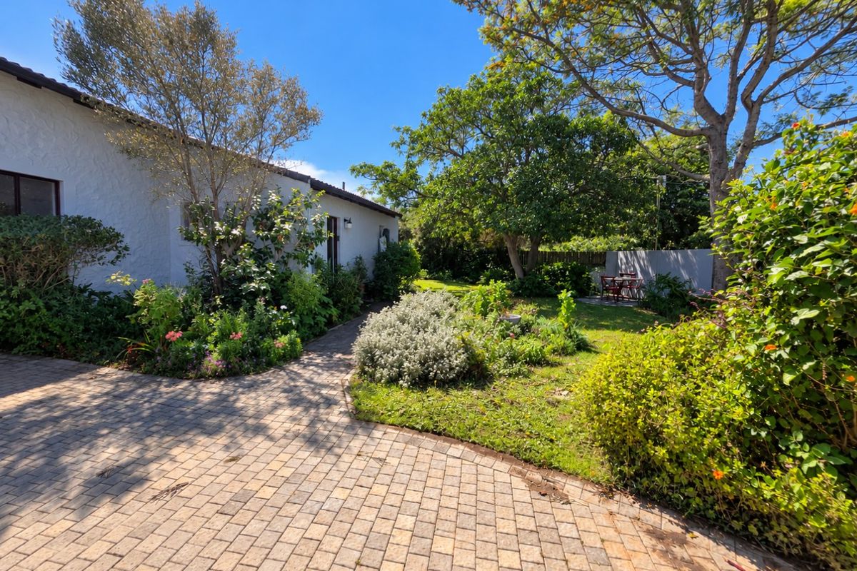 A well-maintained rear garden featuring a paved walkway, mature trees, and established landscaping alongside the side of the house.