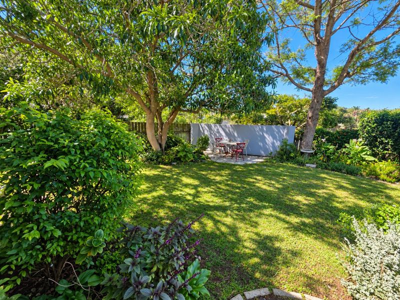 A lush, well-maintained garden featuring mature trees, a paved patio area, and a solid boundary wall for privacy.