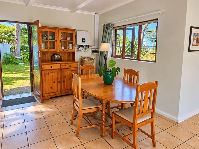 Dining area featuring tiled flooring, exposed ceiling beams, and direct access to the garden through a glass-paneled door.
