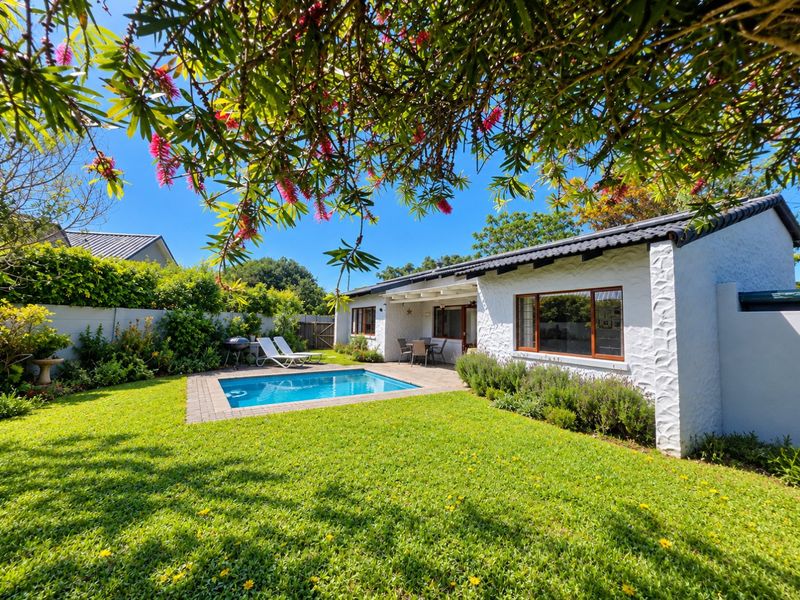 A well-maintained rear garden featuring a swimming pool, paved surround, and a covered patio area attached to the white-walled residence.