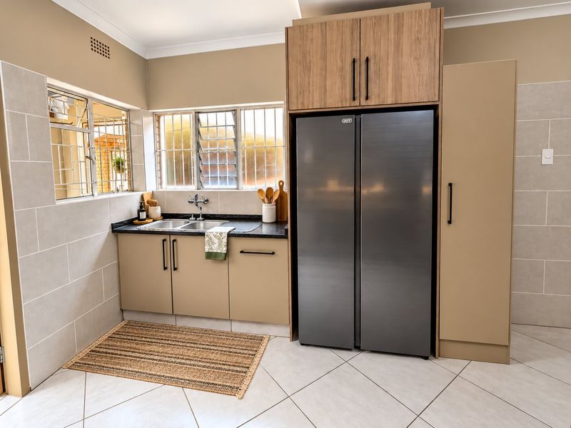 Modern kitchen featuring sleek laminate cabinetry, stone countertops, a double sink, and tiled finishes, offering a clean and functional workspace.