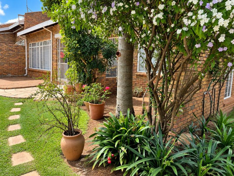 A well-maintained rear garden area featuring a face brick townhouse facade, paved patio space, and established garden landscaping with a stepped path.