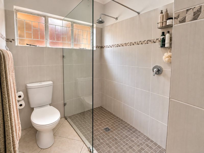 A modern bathroom featuring a spacious walk-in shower with a glass screen, neutral wall tiling, and a standard toilet.