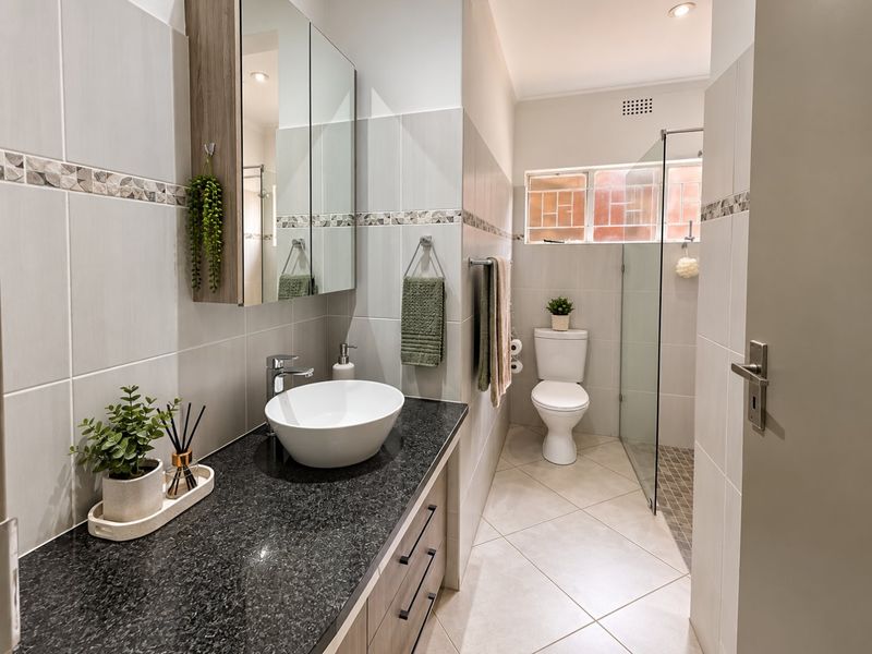 Modern bathroom featuring a vessel sink on a granite vanity, a walk-in shower with glass screen, and neutral wall and floor tiling.
