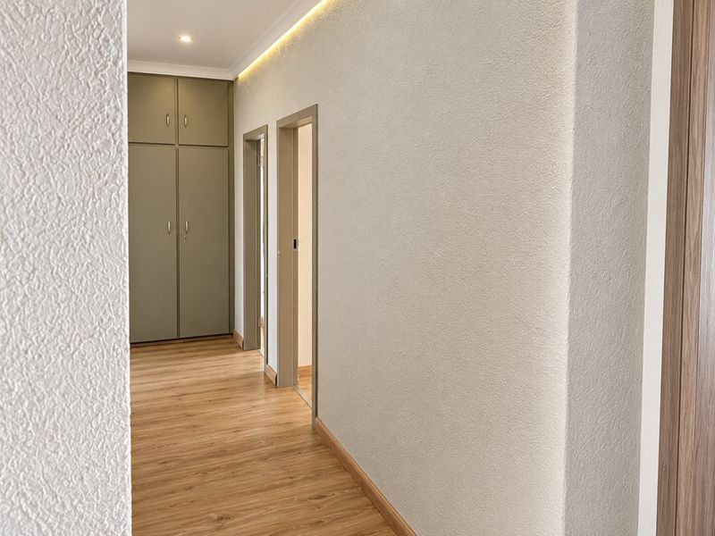 A clean, modern hallway featuring light laminate flooring, recessed ceiling lighting, and built-in storage cupboards.