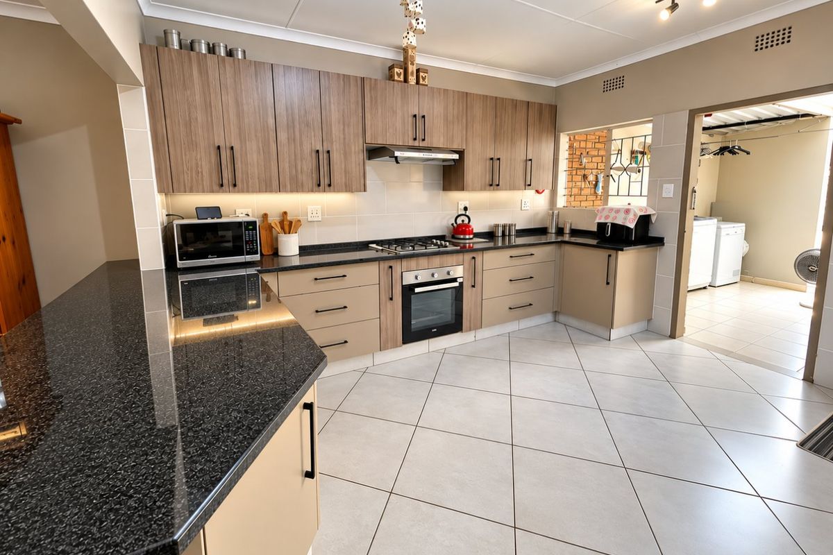 Modern kitchen featuring granite countertops, built-in oven, gas hob, extractor fan, and ample cabinetry, with tiled flooring and an adjacent laundry area.