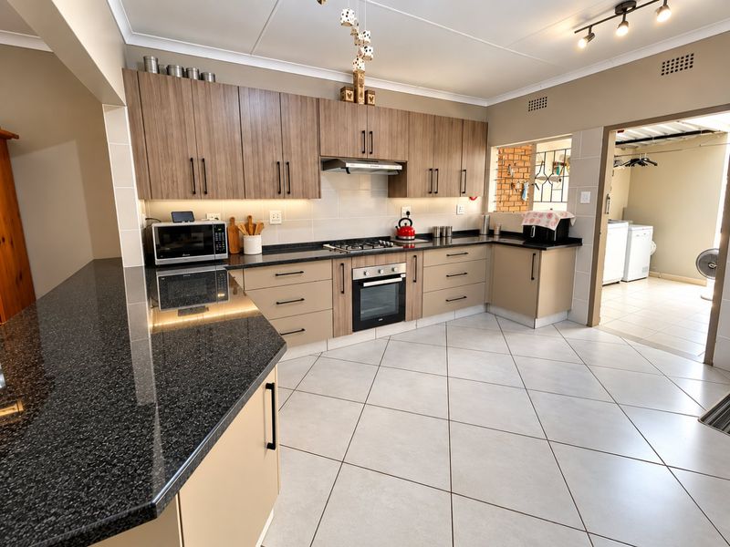 Modern kitchen featuring granite countertops, built-in oven, gas hob, extractor fan, and ample cabinetry, with tiled flooring and an adjacent laundry area.