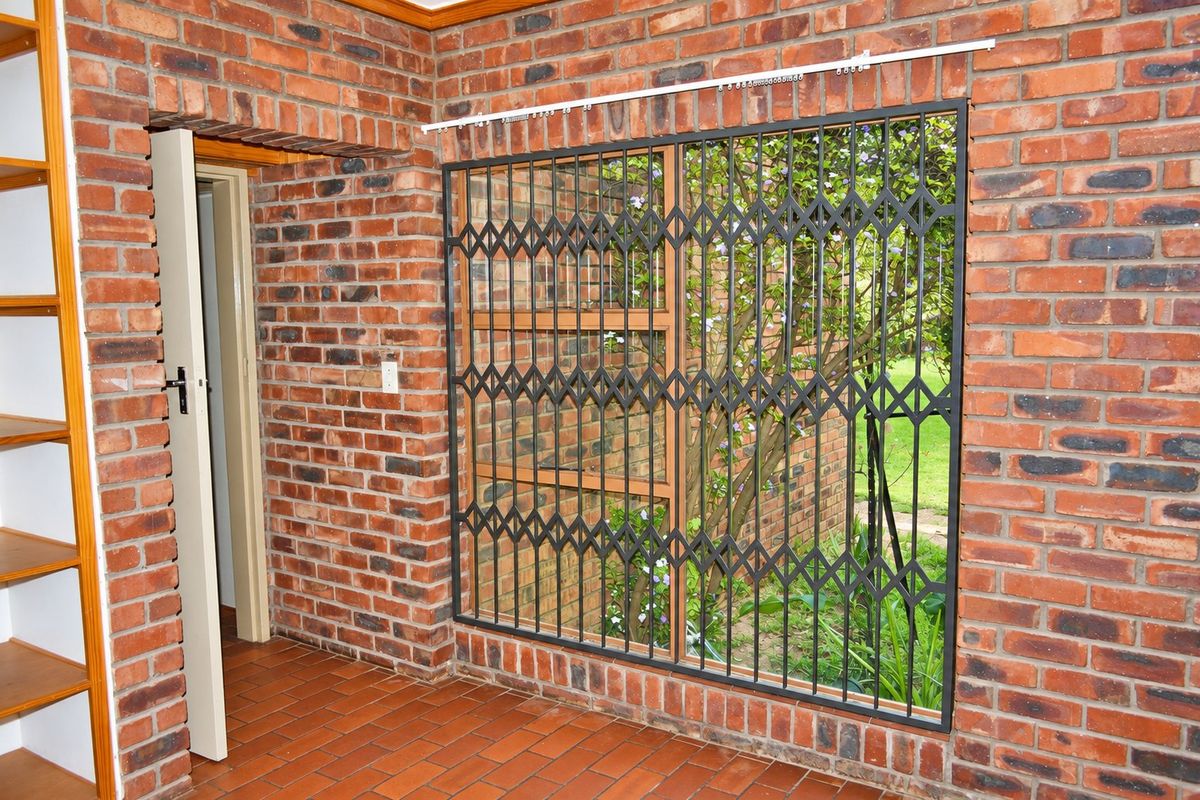An interior living space featuring exposed brick walls, terracotta tile flooring, and built-in wooden shelving, with a secure metal gate over the window.