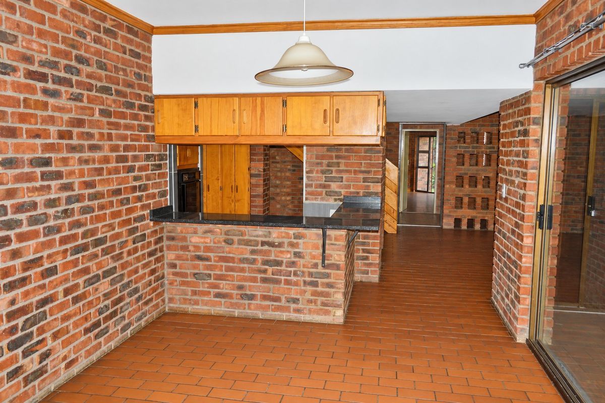 A dated kitchen area featuring exposed brick walls, built-in wooden cabinetry, a brick breakfast bar, and tiled flooring, offering potential for modern renovation.