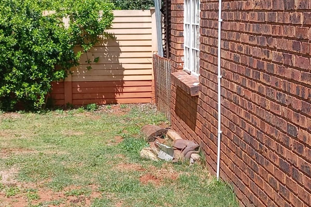 A view of the rear brick exterior wall and garden area, showing a damaged boundary fence and debris along the building perimeter.