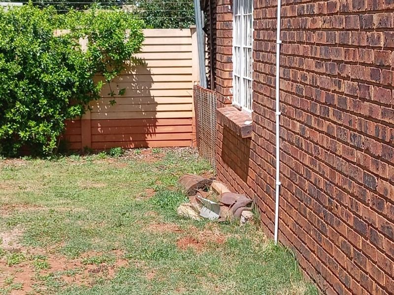 A view of the rear brick exterior wall and garden area, showing a damaged boundary fence and debris along the building perimeter.