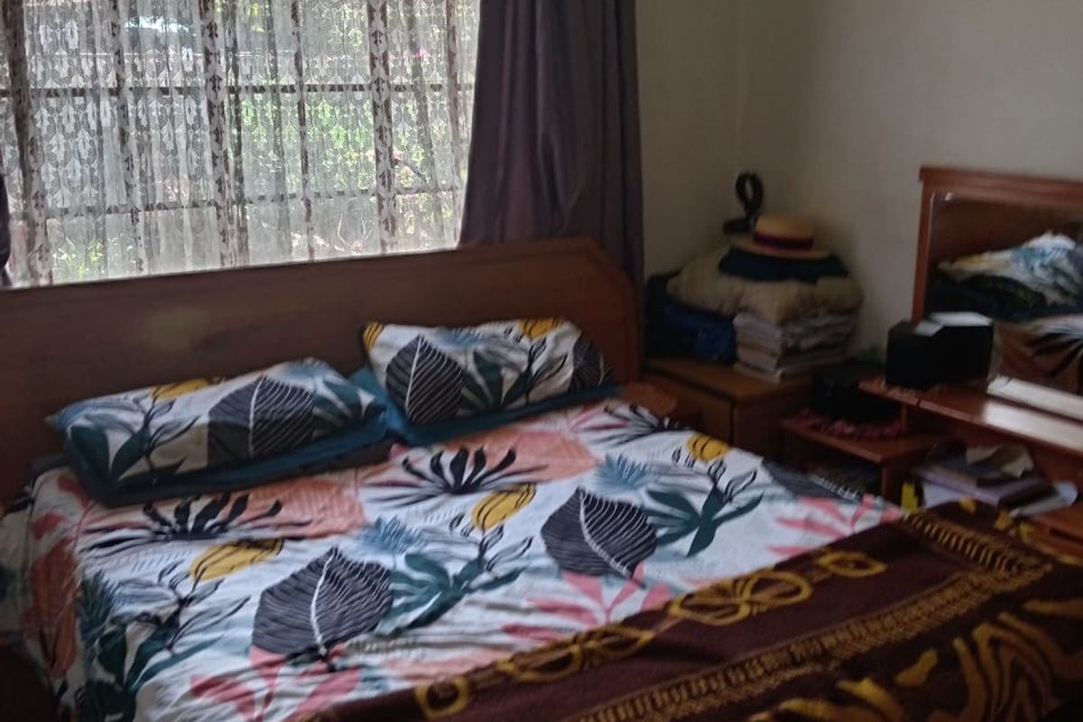 A functional bedroom featuring tiled flooring, a ceiling fan, and a window fitted with security bars.