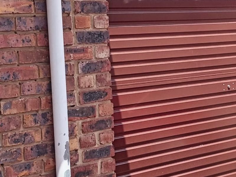 A close-up view of a garage exterior featuring a brown roller shutter door and a face brick wall with a downpipe.
