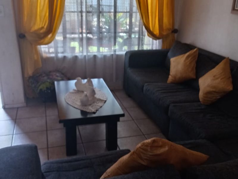 A living room area featuring tiled flooring and a window with security gate, providing a functional space for relaxation.