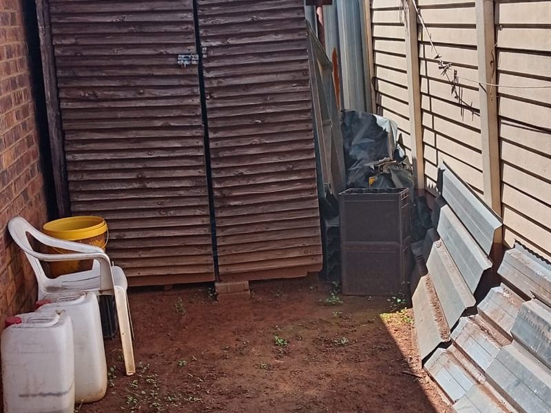 A narrow side yard area featuring a wooden storage shed, brick walling, and precast concrete boundary fencing.