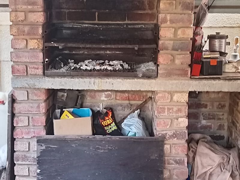 A built-in brick braai area featuring a metal extractor hood and concrete prep surface, suitable for outdoor entertaining.