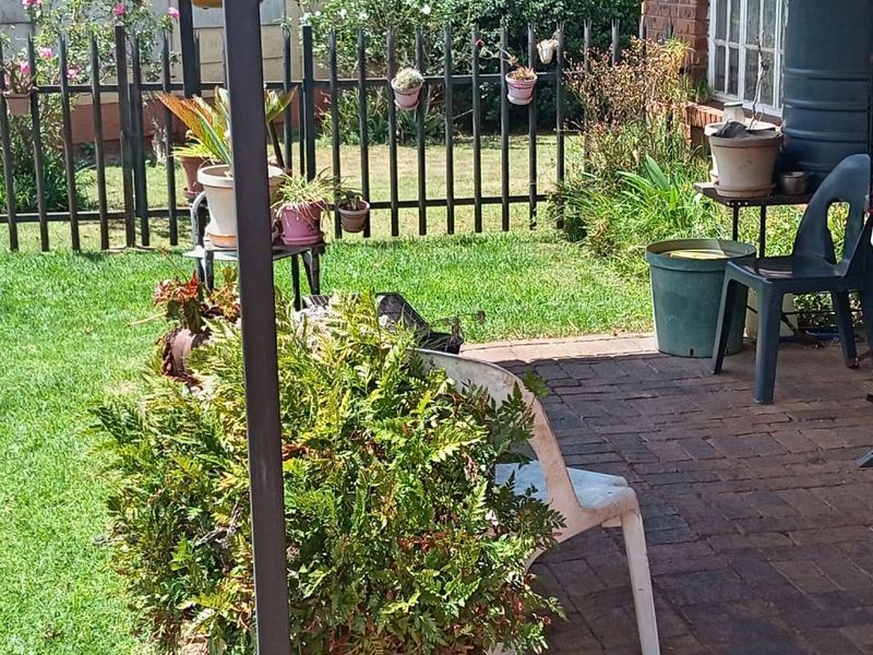 A covered brick-paved patio area overlooking a private garden with metal fencing and a brick exterior wall.