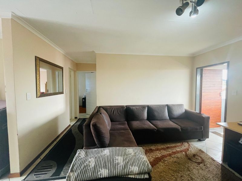 A living room area featuring tiled flooring, coving, and a spotlight fixture, providing access to adjacent rooms and an external entrance.