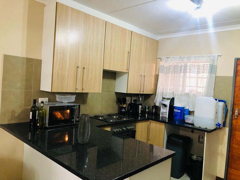 A functional kitchen featuring light wood-finish cabinetry, dark granite countertops, a built-in oven, and an electric hob with a tiled backsplash.