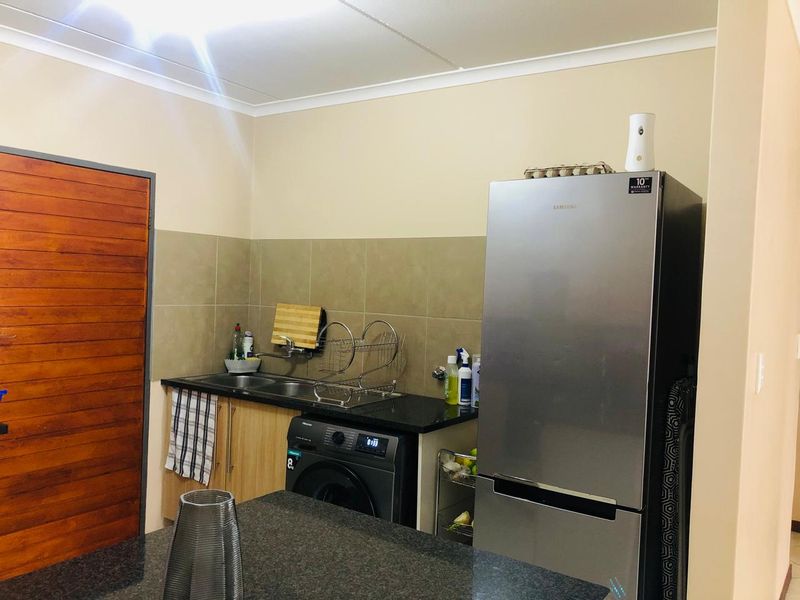 Compact kitchen area featuring granite countertops, a double basin sink, and neutral tiled backsplash with integrated cabinetry.