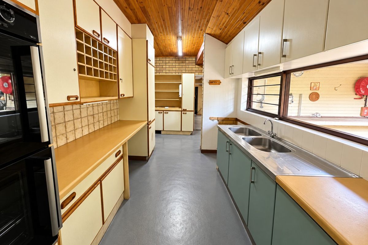 Spacious kitchen featuring extensive built-in cabinetry, double stainless steel sink, built-in oven, and a distinctive timber paneled ceiling.